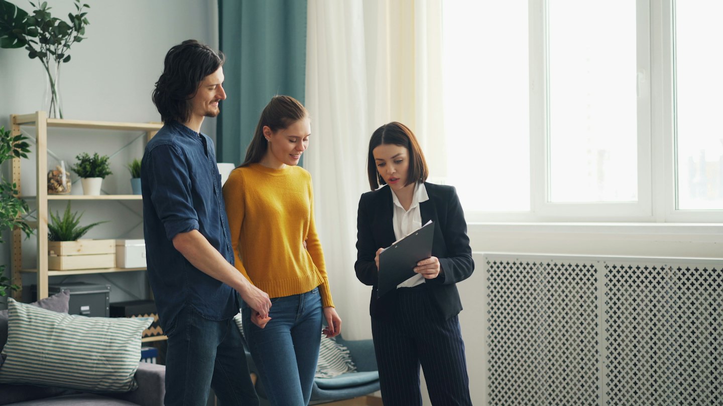 Real estate agent shows documents to a couple in a modern apartment.